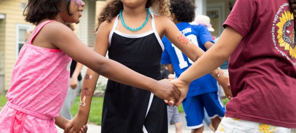Children holding hands in a circle at a Beacon Community Collective gathering