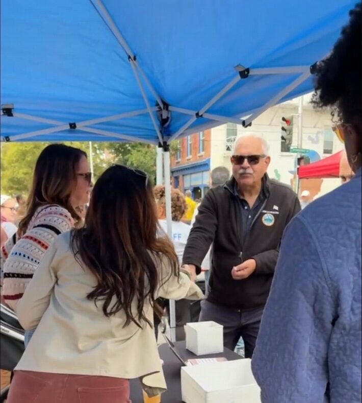 People greeting each other under a blue tent at the Spirit of Beacon Day street fair